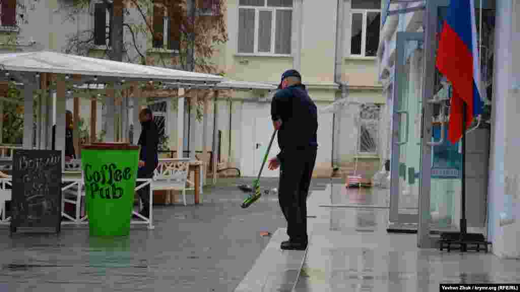 Мужчина убирает со ступеней яхтклуба воду и листья